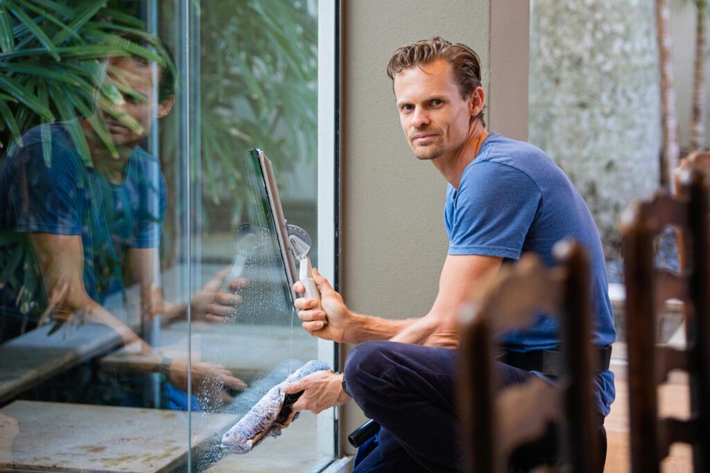 pexels-photo-634007-634007 A man in a blue t-shirt cleaning large glass pane with a squeegee indoors.